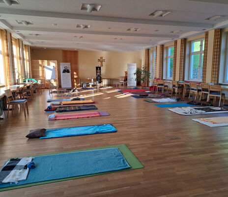Ein großer Raum mit Parkettboden. Mehrere Gymnastikmatten mit Decken liegen verteilt im Raum.