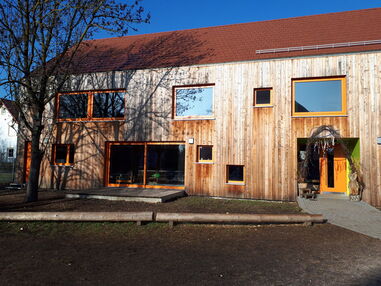 Ein holzverschaltes Haus mit großen Fenstern.