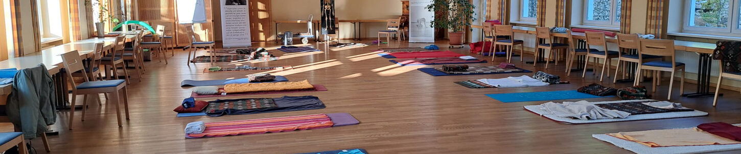 Ein großer Raum mit Parkettboden. Mehrere Gymnastikmatten mit Decken liegen verteilt im Raum.